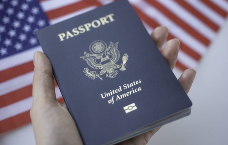 fingers holding Passport of USA on blurred American flags background. Close up view